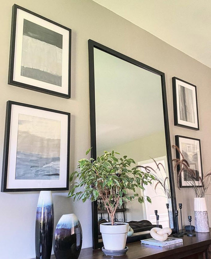 Neutral DIY Abstract Art with a sleek, black frame on the wall of a living room. surrounded by a black framed mirror and greenery.