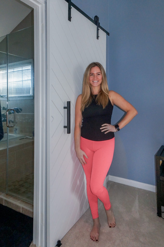 Blonde woman standing next to a DIY Modern Barn Door, white trim with black hardware against a blue wall. 