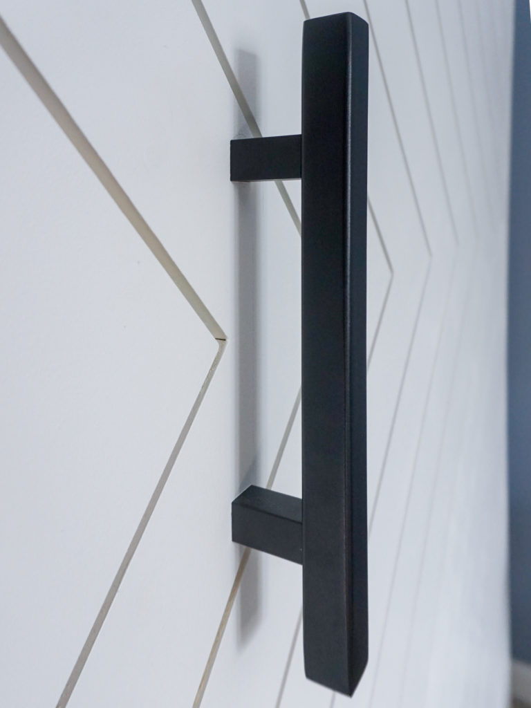 Chunky black door handle on a herringbone white barn door.
