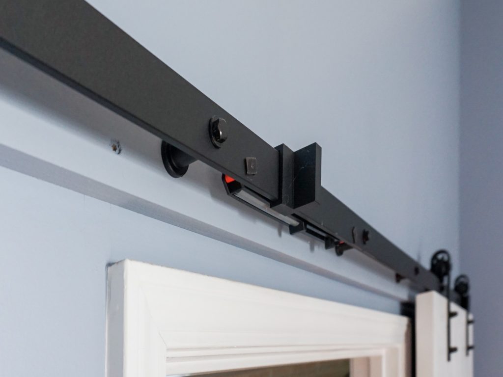 Modern barn door sliding hardware in black, attached to white trim door against a blue wall.