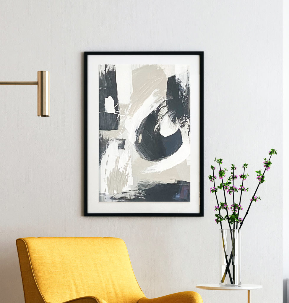 Navy, white and gray Abstract Painting in a modern black frame , hung above a vintage yellow armchair and a small bouquet of pink flowers.