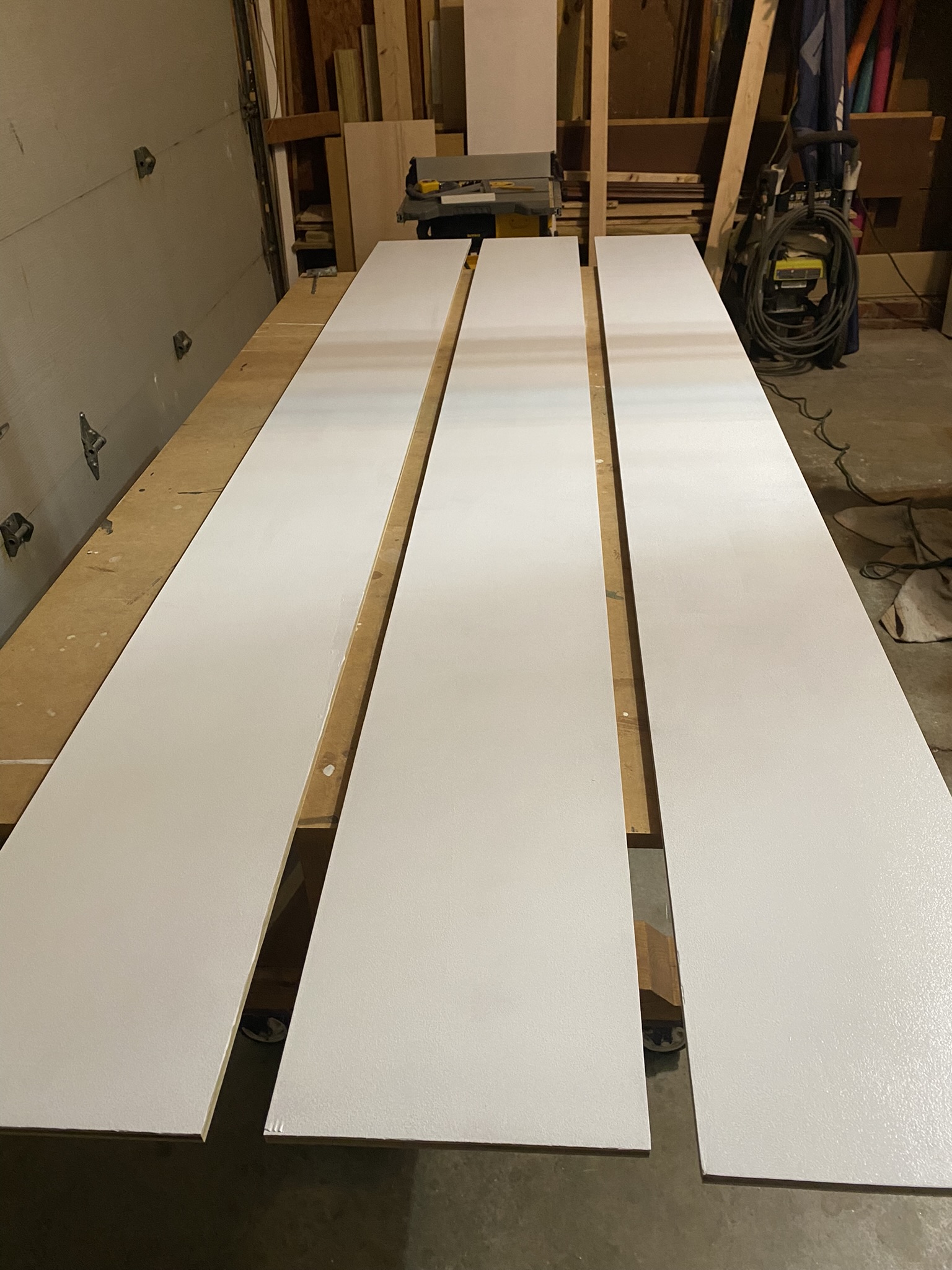 3 wooden panels painted creamy white, drying in a garage.